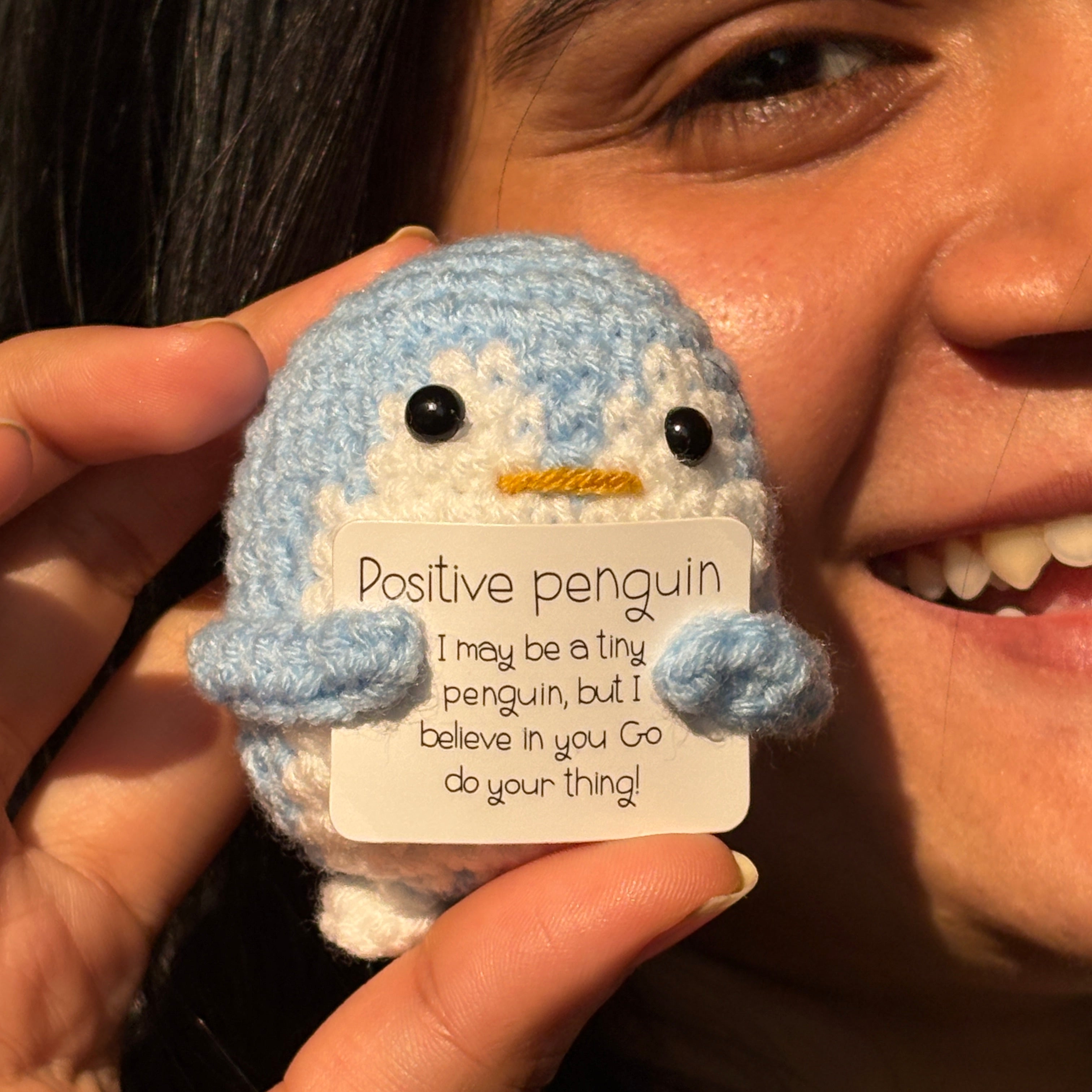 Person holding a small plush penguin with a tag labeled 'Positive Penguin' near their face.
